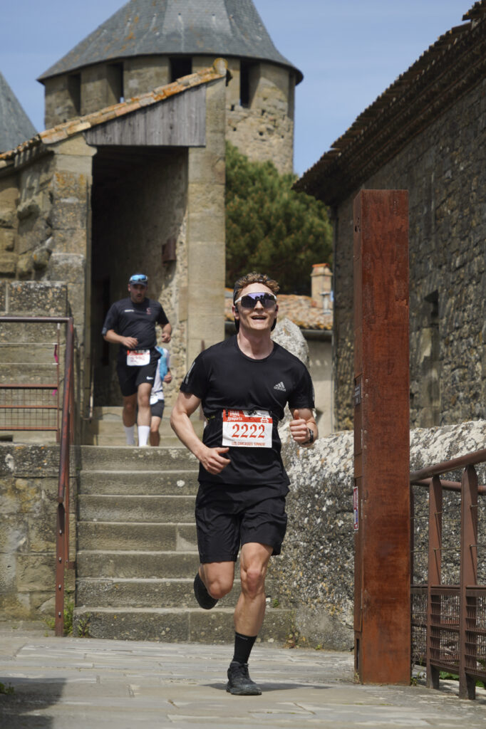 Un coureur de trail équipé descendant les marches historiques des fortifications de la Cité de Carcassonne.
