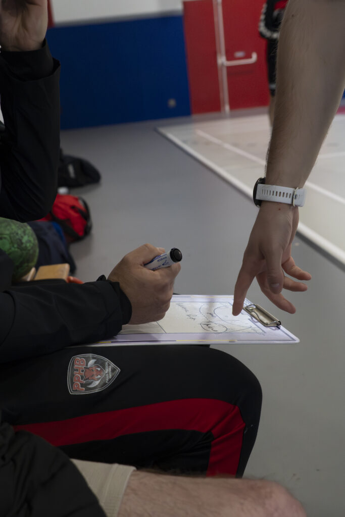 Détail d'une main d'entraîneur de handball expliquant la tactique de jeu sur une plaquette lors d'un temps mort.