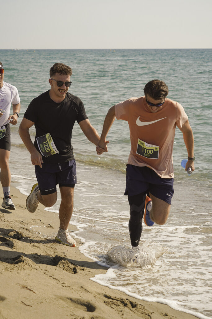 Solidarité sportive : deux coureurs se tenant la main en pleine action sur le sable du Biquet Trail.