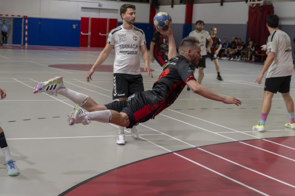 Plongeon et tir horizontal d'un joueur noir et rouge pendant un match de handball près de Carcassonne.