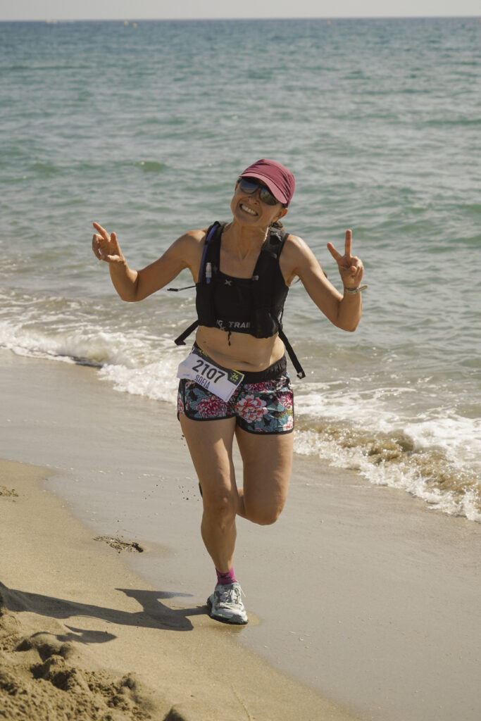 Reportage photo sportif au Biquet Trail : une runneuse saluant l'objectif au bord de l'eau.